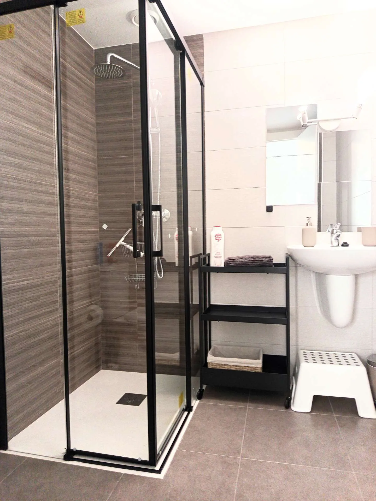 Łazienka z kabiną prysznicową w czarnych ramach, umywalką i regałem